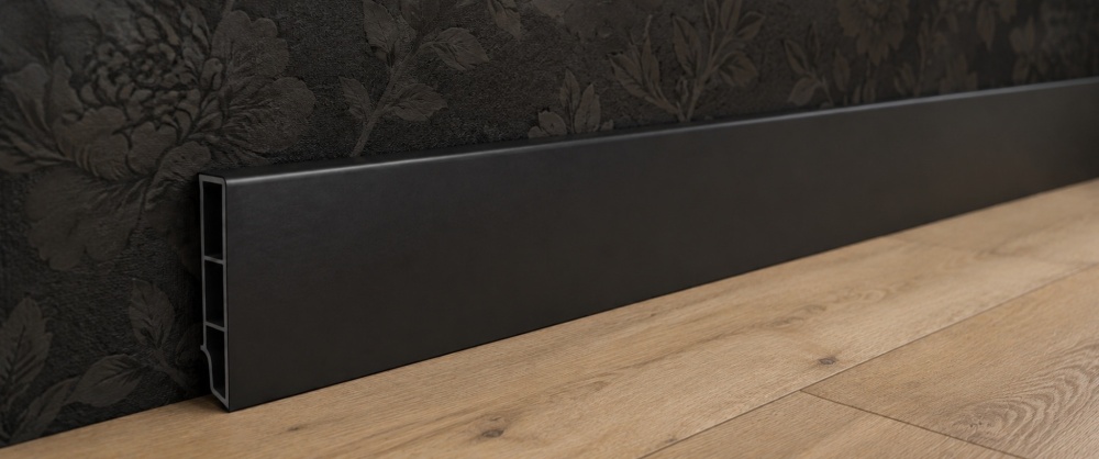 Zwarte kunststof plint tegen donkere wand met houten vloer
